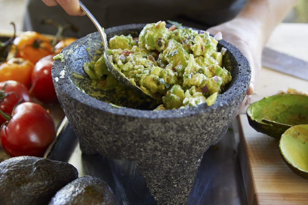 hand scooping guacamole out of a bowl with a spoon