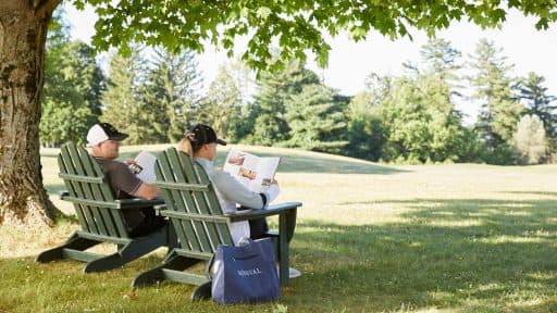 two people sitting on green chairs reading a book outside