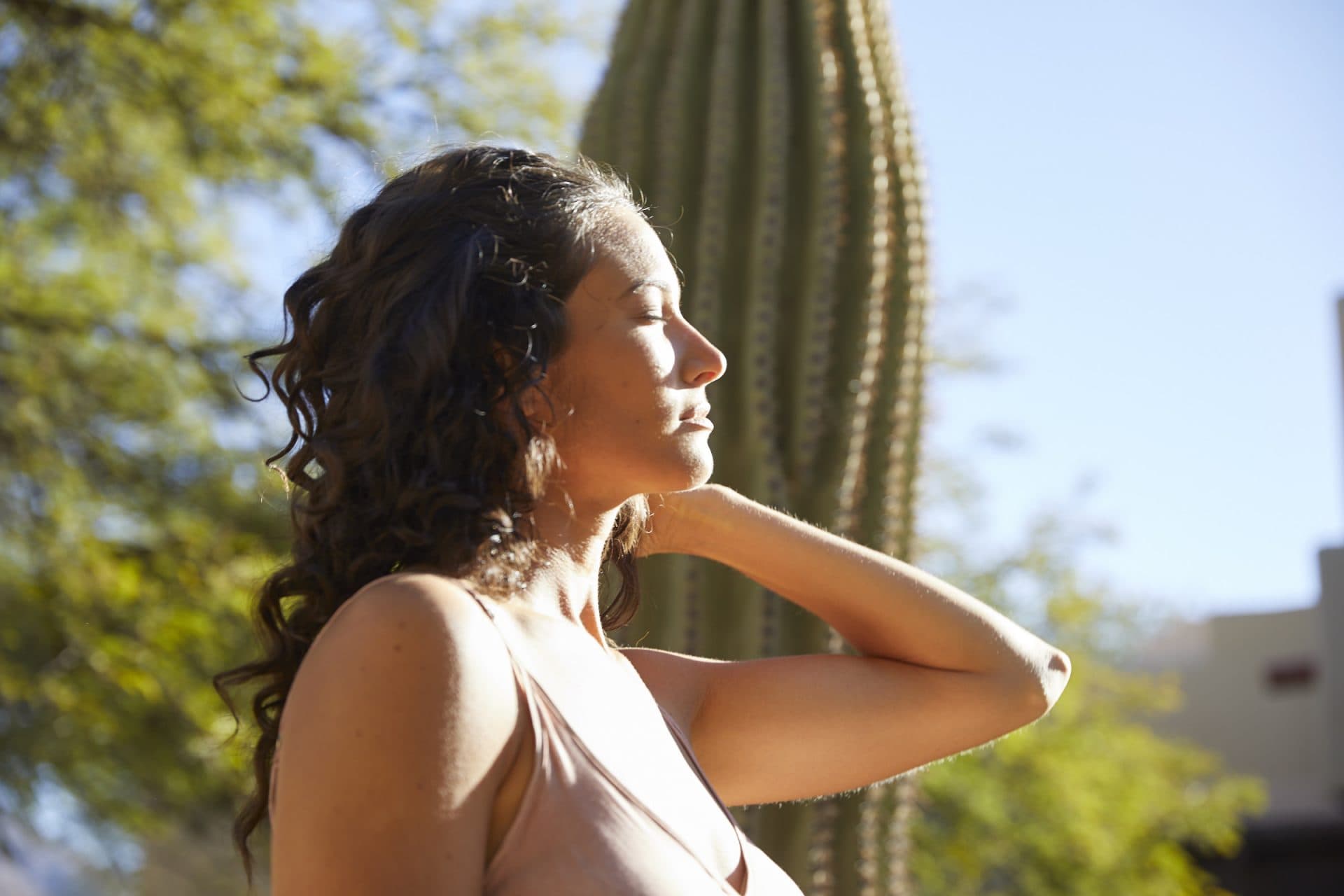 Woman with closed eyes standing relaxed in the sun in front of big cactus