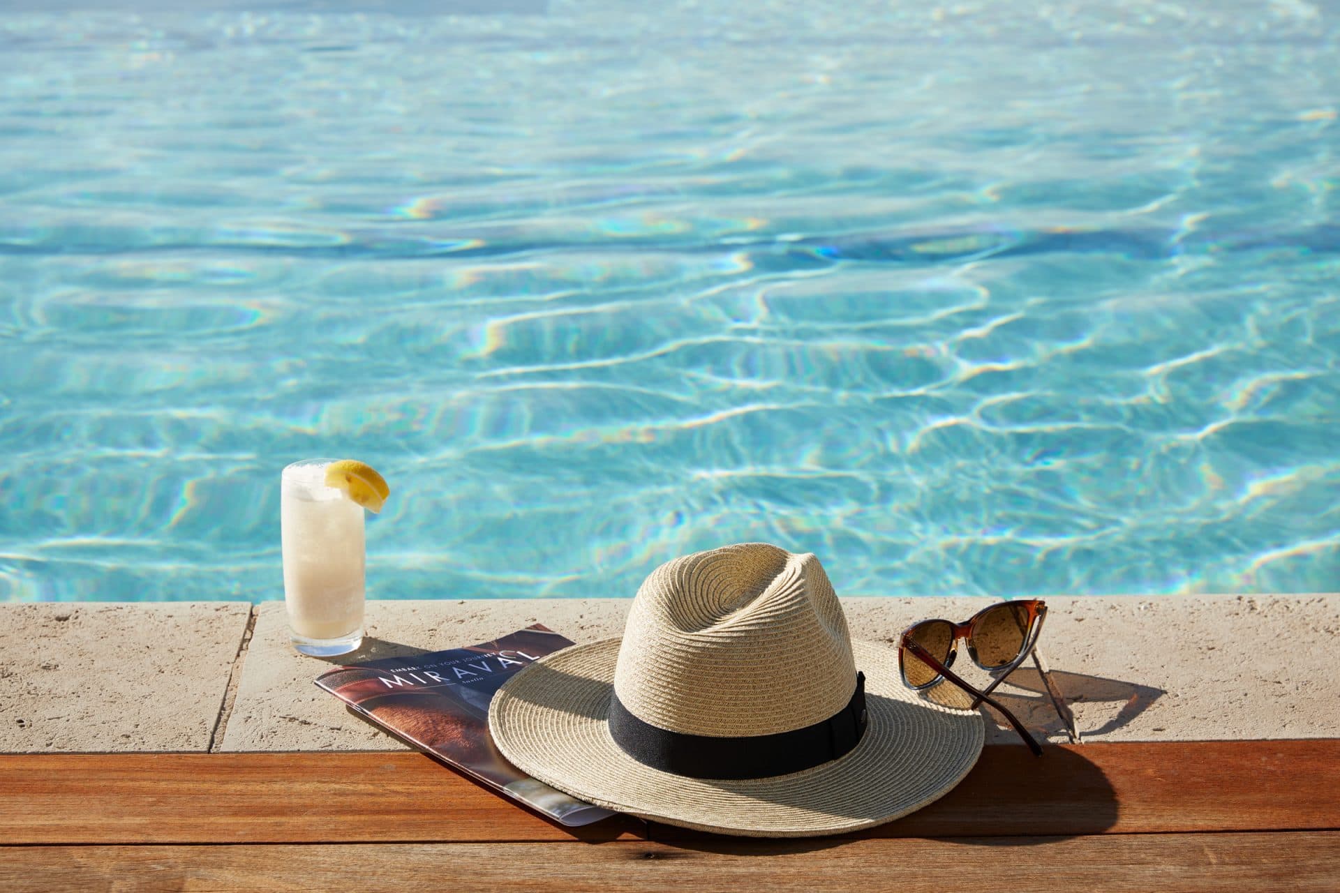 A drink, hat and sunglasses on the side of a pool