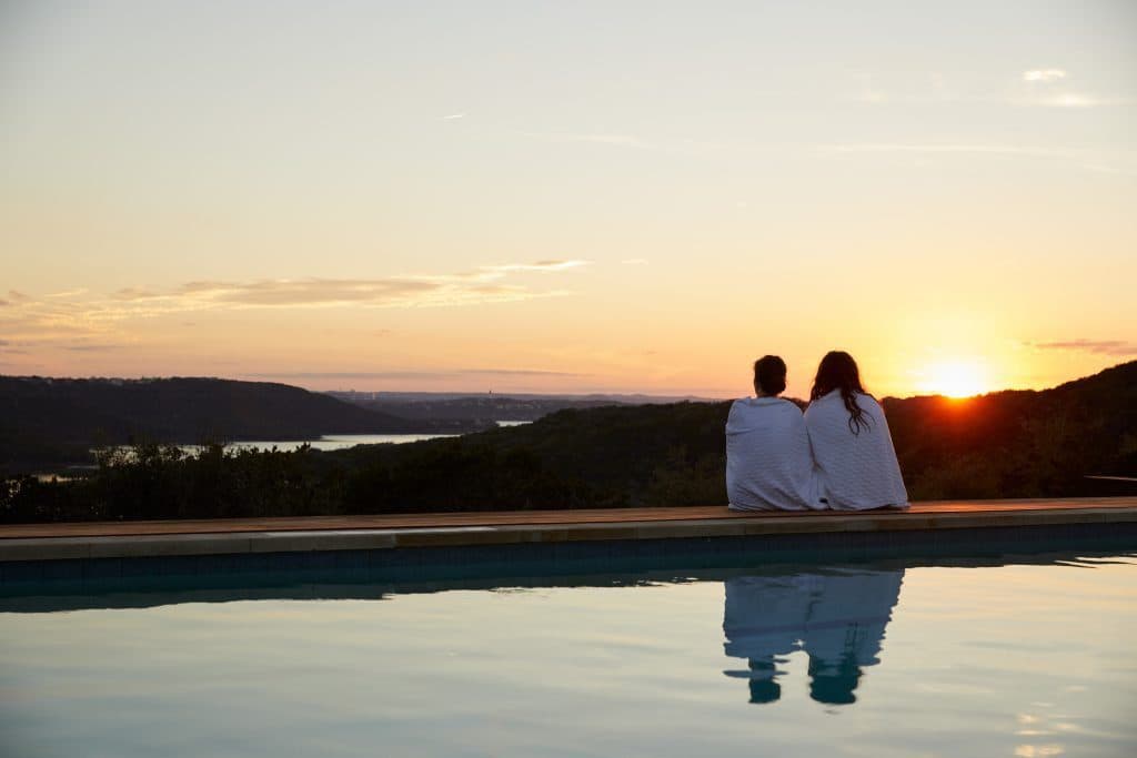 two people in robes sitting by the pool watching the sunset