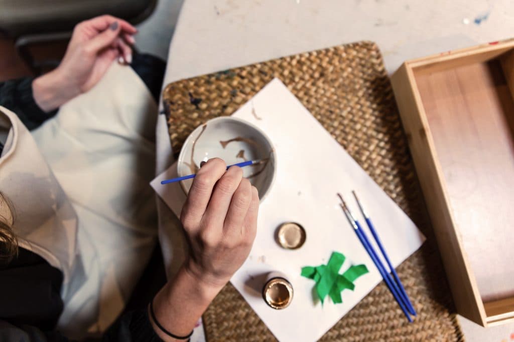 Person with paint brush decorating white bowl with gold paint
